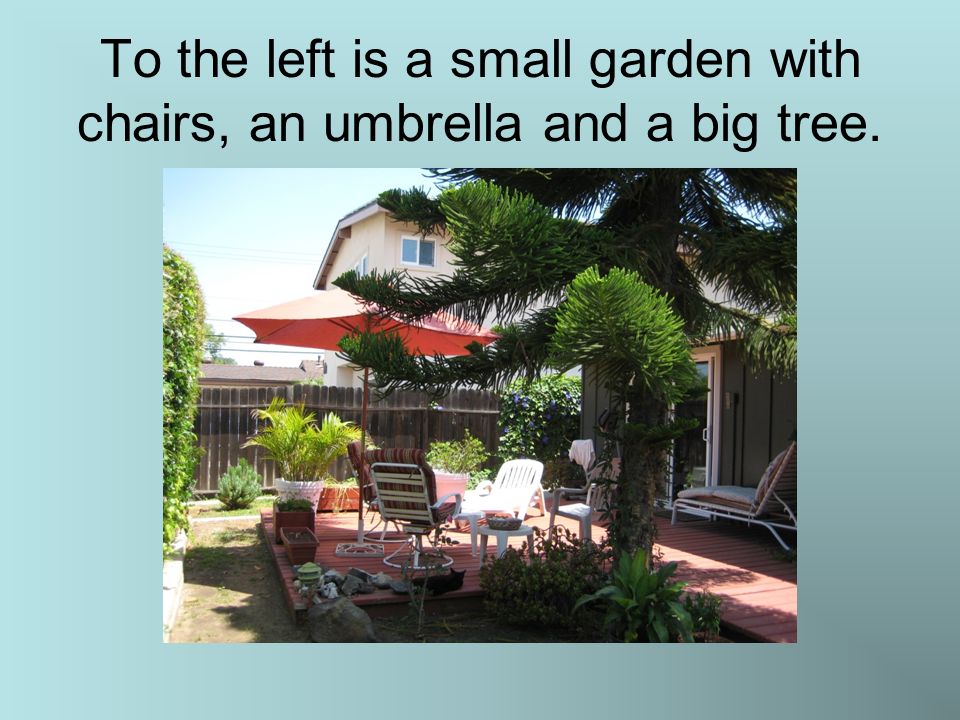 To the left is a small garden with chairs, an umbrella and a big tree.