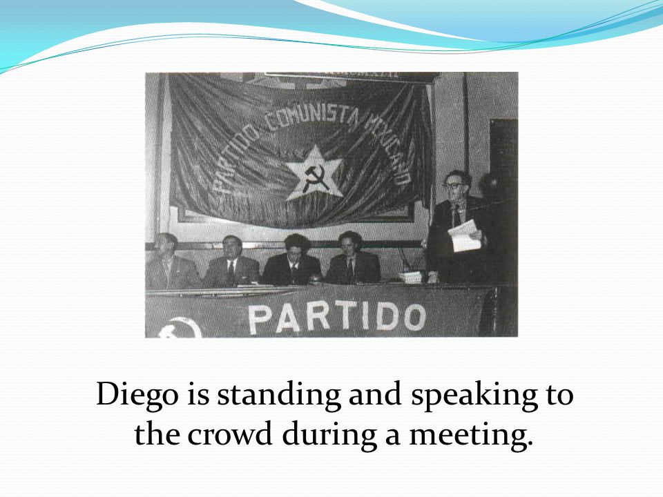 Diego is standing and speaking to the crowd during a meeting.